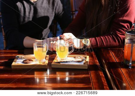 Couple Sitting Near Table With Sea-buckthorn Broth In Glass Cups Jug Cutlery In Cafe Discuss Film, Y