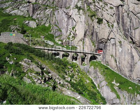 Red Express Train On Scenic Stony St. Gotthard Railway Bridge And Tunnel, Swiss Alps, Switzerland