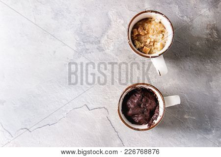Chocolate And Vanilla Caramel Mug Cakes From Microwave Over Grey Texture Background. Top View, Copy 