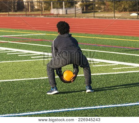 A High School Track And Field Athlete Is Squatting Down Ready To Throw A Medicine Ball Over His Head