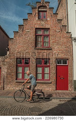 Bruges, Belgium - July 05, 2017. Brick Old House And Cyclist In Bruges. With Many Canals And Old Bui