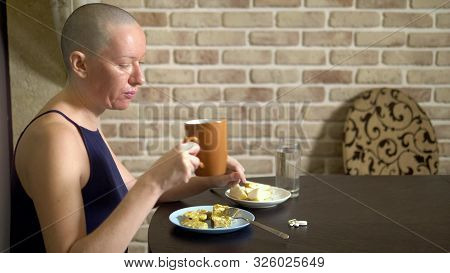 Proper Nutrition After Chemotherapy. A Bald Woman At The Table Drinks Pills While Eating.