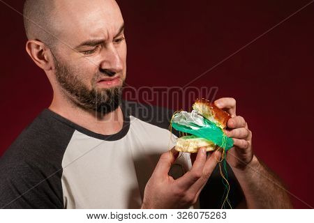 The Concept Of Fast Food And Ecology. A Bald Man With A Beard Looks Disgustedly Into The Plastic Fil
