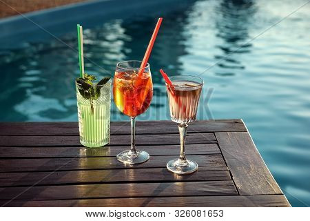 Glasses Of Fresh Summer Cocktails On Wooden Table Near Swimming Pool Outdoors
