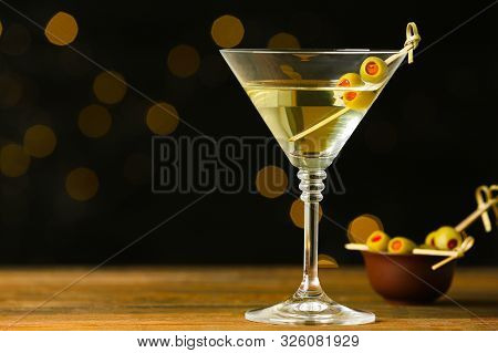 Glass Of Classic Dry Martini With Olives On Wooden Table Against Blurred Background. Space For Text