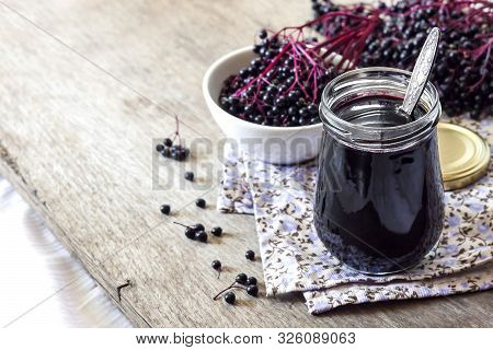 Homemade Black Elderberry Syrup In Glass Jar And Bunches Of Black Elderberry In Background, Copy Spa