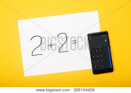 Paper With Written Task 2 Plus 2 And With A Solution On Smartphone Screen On Yellow Background. Educ