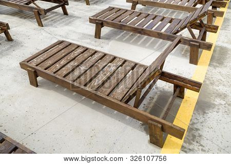 Row Of Empty Wooden Beach Chairs Near Water Outdoors.