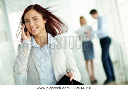 Menina bonita no desgaste formal falando em seu telefone móvel, seus colegas segurando uma discussão no b