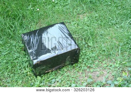 A Parcel In A Black Box Lying On The Grass. Curier Posts. Receiving Parcels.