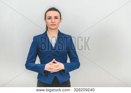 Serious Young Teacher Standing, With Her Fingers Interlaced, Looking Confidently At The Camera.