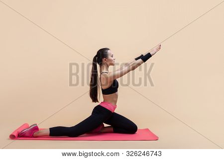 Young Attractive Girl With A Ponytail, Brunette, Sitting In The Pose Of A Pigeon With His Hands On A