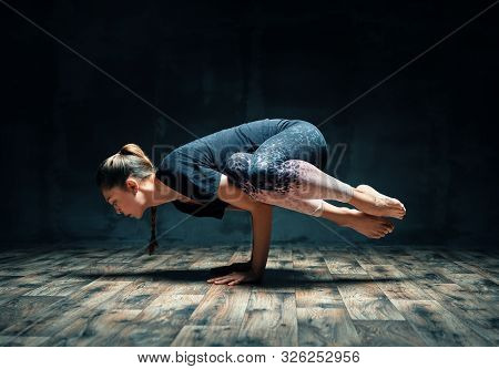 Young Attractive Woman Practicing Yoga Doing Side Crane Pose In Dark Room. Parsva Bakasana Exercise.