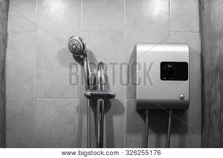 Instant Tankless Electric Water Heater Installed On Grey Tile Wall With Input And Output Pipe Outlet