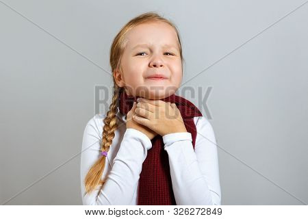 A Little Girl In A Scarf Suffers From A Sore Throat. The Child Holds On To The Neck. The Concept Of 
