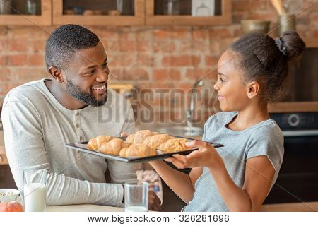 Adorable Black Girl Showing Dad Just Baked Croissants, Father Smiling, Kitchen Interior, Copy Space