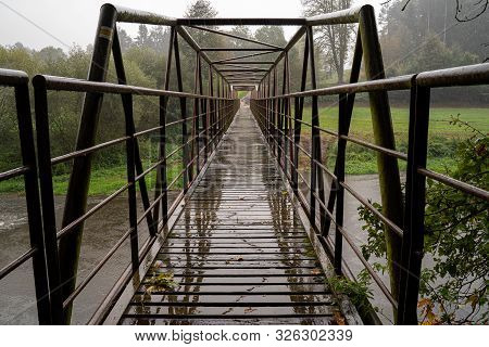 Steel Bridge With Wooden Walkpath. Crossing River In Bad Weather.