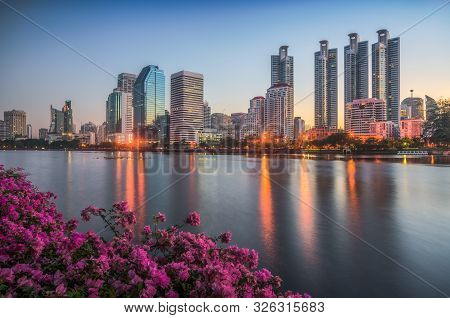 Lake With Purple Flowers In City Park Under Skyscrapers At Sunrise. Benjakiti Park In Bangkok, Thail