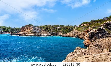 Houses On Cliffs Around Beautiful Beach, Cala Llombards In Mallorca, Turquoise Water And Blue Sky, B