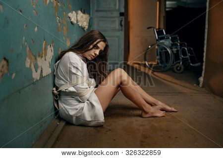 Mad patient in straitjacket sitting on the floor
