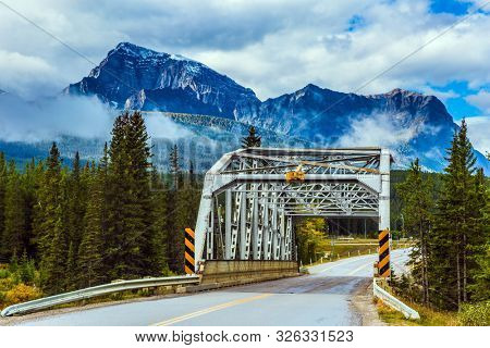 Trellised bridge across the river. Evergreen forest grows along the side of the road. Cloudy fall day in the Canadian Rockies. Concept of active, eco and photo tourism