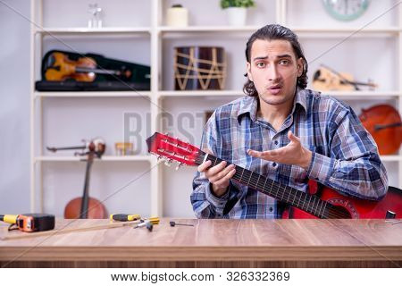 Young handsome repairman repairing guitar