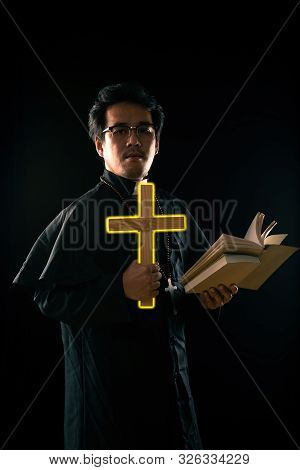 Dark Tone, Rim Light - Priest Show Lighting Crucifix While Holding Bible To Exorcise Ghost On Black 