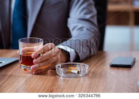 Male employee drinking alcohol and smoking cigarettes at workpla