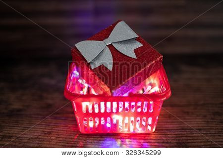 Christmas Present Box With Bow And Glitters Inside Shopping Basket With Colorful Festive Fairy Light