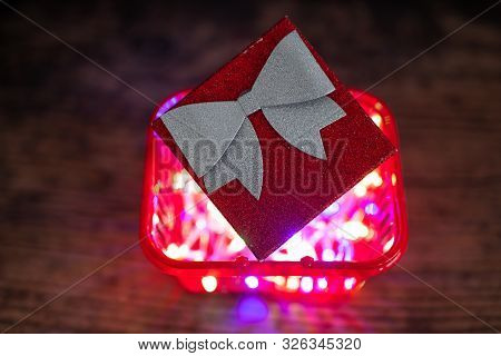 Christmas Present Box With Bow And Glitters Inside Shopping Basket With Colorful Festive Fairy Light
