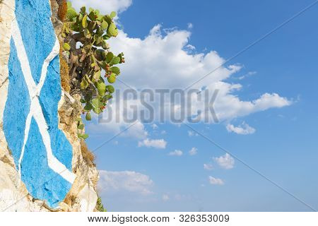 Rock Retaining Wall And Around Coastline At Nafplio With Greek Flag And Prickly Pear Cactus Against 