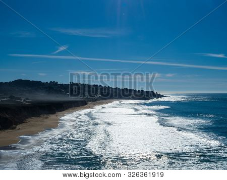 Beach View Of Heavy Waves And Clear Skies With Some Surfers