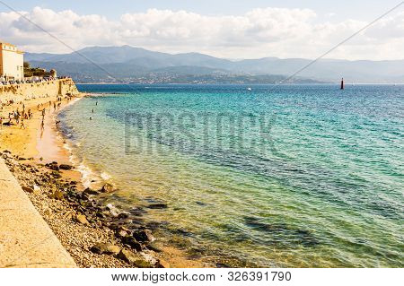 Ajaccio Public Beach With Tourists At Sunny Day. Summer Landscape Of Corsica Island At Sunny Summer 