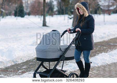 Beautiful Mother Walking In The Park With Her Little Baby In Stoller. Woman Dressed In Blue Jaket Wi