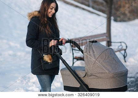 Young Mother Walking With Her Baby In Pram. Beautiful Stoller. Winter Photosession