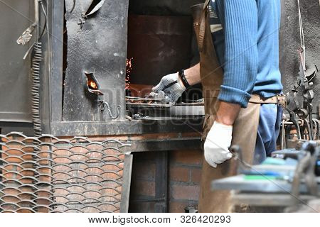 Blacksmith Heats Iron In A Furnace. Young Traditional Blacksmith Working With Open Fire The Blacksmi