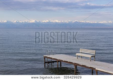 Pier With Benches On Lake Issyk-kul With A Mountain Range With Snow-capped Peaks On The Horizon Agai