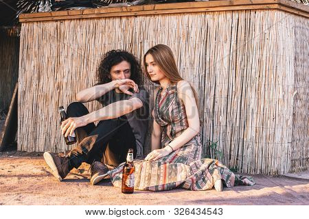 Cute, Hipster Couple Sitting On The Ground, Drinking Beer, Guy Whispering Something To His Girl