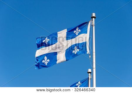 Quebec Flag Waving In The Wind Against Blue Sky In Quebec City.