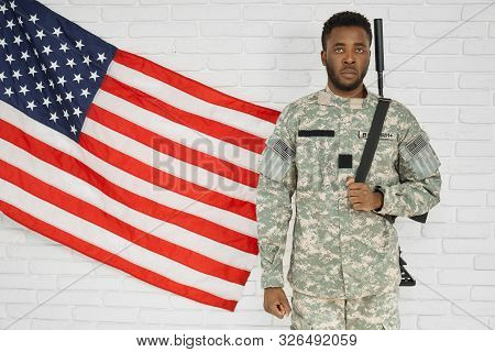 Front View Of American Soldier Wearing Green Uniform Standing Near National Flag On Brick Wall And L