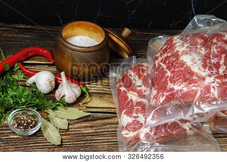 Meat Packed In Vacuum Bags And Seasoning On Wooden Background.