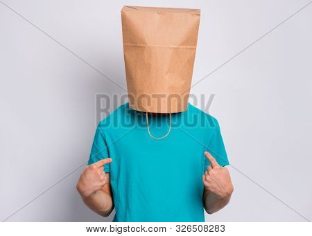 Portrait of teen boy with paper bag over head making fingers up gesture. Teenager cover head with bag pointing fingers on himself. Child pulling paper bag over head posing in studio.