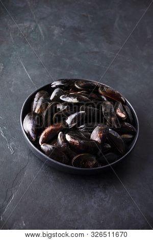 Bowl with fresh raw mussels on dark background