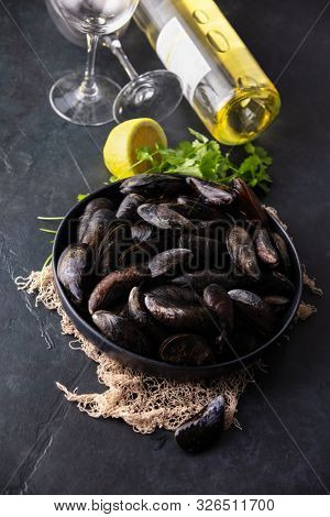 Bowl with fresh raw mussels on dark background