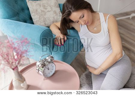 Pregnant Woman Sitting On The Floor And Relaxing At Home, Expecting Her Baby, Cuddling Her Belly And
