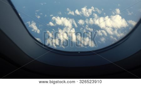 View From The Porthole Of An Airplane On A Blue Sky And Clouds. Airplane Wing Through The Porthole. 