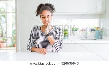 Beautiful african american woman with afro hair wearing casual striped sweater touching mouth with hand with painful expression because of toothache or dental illness on teeth. Dentist concept.