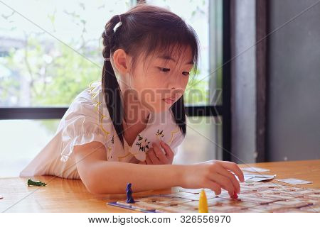 A Attractive Little Asian Girl Deep In Thought As She Contemplates Her Next Move In A Board Game.