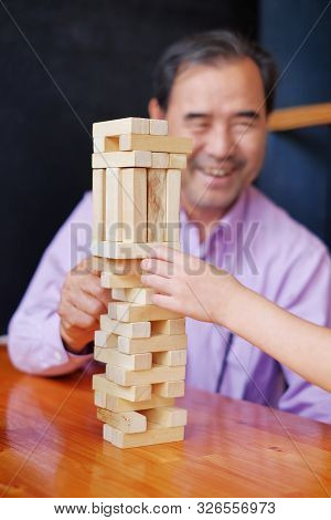 An Grandfather Is Teaching His Granddaughter To Play A Block Wood Tower Game.