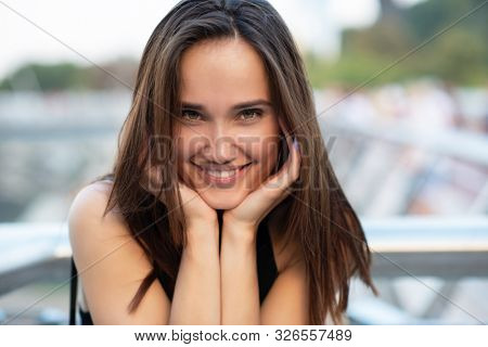 Young pretty likable cheerful woman posing summer city outdoor in Kyiv, Ukraine. Beautiful self-confident girl with long brown hair posing on Dnipro river bank enjoing her life, urban lifestyle